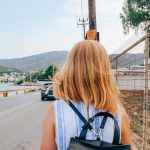 Back view of a woman walking by the coastline in Porto Rafti, Greece, with mountains in the background.