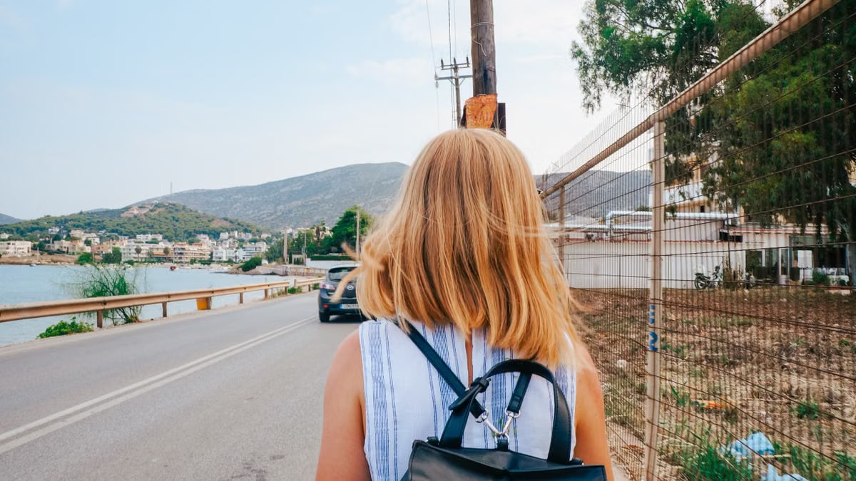 Back view of a woman walking by the coastline in Porto Rafti, Greece, with mountains in the background.